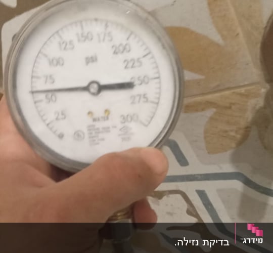 מד לחץ מים מוחזק ביד על רקע אריחים